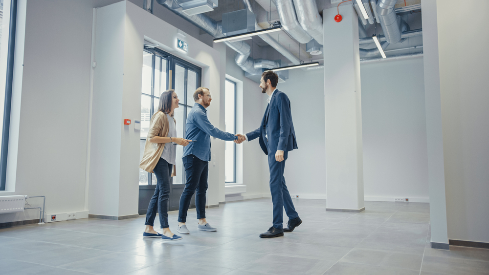 Real Estate Agent Showing a New Empty Office Space to Young Male and Female Hipsters. Entrepreneurs Meet the Broker and They Shake Hands. They Wish to Purchase or Rent.